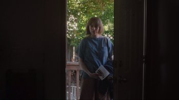 Movie still from “Showing Up” (2022), directed by Kelly Reichardt – A woman standing in front of a door holding a book; Medium shot, Over the shoulder angle