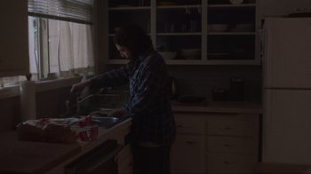 Movie still from “Showing Up” (2022), directed by Kelly Reichardt – A person in a kitchen washing dishes in a sink; Medium shot, Low angle