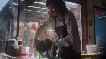 Movie still from “Showing Up” (2022), directed by Kelly Reichardt – A woman wearing an apron and holding a frying pan; Medium shot, Low angle