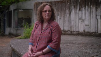 Movie still from “Showing Up” (2022), directed by Kelly Reichardt – An older woman sitting on the ground in front of a building; Medium shot, Over the shoulder angle