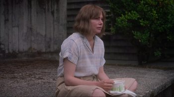 Movie still from “Showing Up” (2022), directed by Kelly Reichardt – A woman sitting on the ground holding a cup; Medium shot, High angle