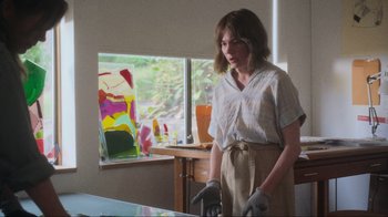 Movie still from “Showing Up” (2022), directed by Kelly Reichardt – A woman standing in front of a painting in a room; Medium shot, Low angle