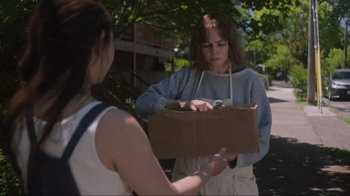 Movie still from “Showing Up” (2022), directed by Kelly Reichardt – A woman holding a cardboard box while another woman looks on; Medium shot, Over the shoulder angle