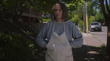 Movie still from “Showing Up” (2022), directed by Kelly Reichardt – A woman standing on a sidewalk wearing an apron; Medium shot, Low angle
