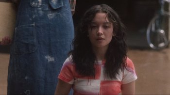 Movie still from “Showing Up” (2022), directed by Kelly Reichardt – A woman with long black hair wearing a red and white shirt; Medium shot, Low angle