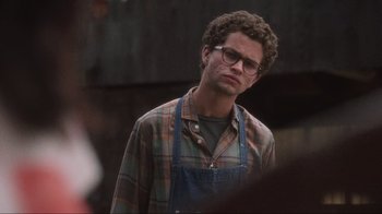 Movie still from “Showing Up” (2022), directed by Kelly Reichardt – A man in a plaid shirt wearing a blue apron; Close Up shot, Over the shoulder angle