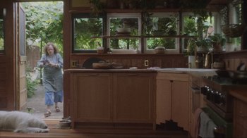 Movie still from “Showing Up” (2022), directed by Kelly Reichardt – A woman standing in a kitchen next to a sink; Wide shot, Low angle