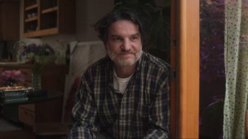 Movie still from “Showing Up” (2022), directed by Kelly Reichardt – A man sitting in a living room wearing a plaid shirt; Close Up shot, Low angle