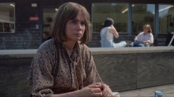Movie still from “Showing Up” (2022), directed by Kelly Reichardt – A woman sitting on a bench in front of a building; Close Up shot, Over the shoulder angle
