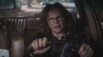 Movie still from “Showing Up” (2022), directed by Kelly Reichardt – An older woman wearing glasses driving in a car; Close Up shot, Over the shoulder angle