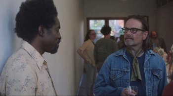 Movie still from “Showing Up” (2022), directed by Kelly Reichardt – Two men are standing in a hallway talking; Medium shot, Over the shoulder angle