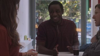 Movie still from “Showing Up” (2022), directed by Kelly Reichardt – A man sitting at a table with a glass of wine; Medium shot, Over the shoulder angle