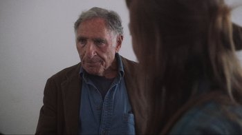 Movie still from “Showing Up” (2022), directed by Kelly Reichardt – An older man looking at a woman in the mirror; Close Up shot, Over the shoulder angle