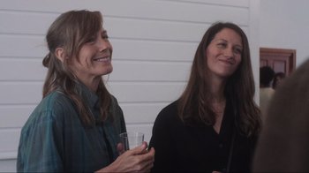 Movie still from “Showing Up” (2022), directed by Kelly Reichardt – Two women standing next to each other holding drinks; Medium shot, Over the shoulder angle