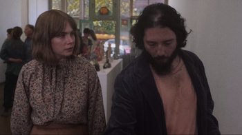 Movie still from “Showing Up” (2022), directed by Kelly Reichardt – A man and a woman standing next to each other in a room; Medium shot, Over the shoulder angle