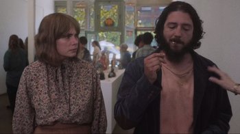 Movie still from “Showing Up” (2022), directed by Kelly Reichardt – A woman standing next to a man in a room; Medium shot, Low angle