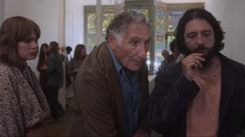 Movie still from “Showing Up” (2022), directed by Kelly Reichardt – An older man sitting next to a woman in a room; Medium shot, Over the shoulder angle