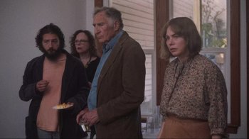 Movie still from “Showing Up” (2022), directed by Kelly Reichardt – A group of people standing next to each other in a room; Medium shot, Over the shoulder angle