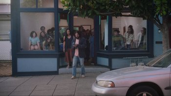 Movie still from “Showing Up” (2022), directed by Kelly Reichardt – A man standing on the side of the street in front of a building; Wide shot, High angle