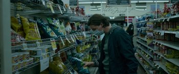Movie still from “Sick” (2022), directed by John Hyams – A person wearing a face mask looking at food in a store; Medium shot, Low angle