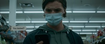 Movie still from “Sick” (2022), directed by John Hyams – A man wearing a face mask while looking at his cell phone; Close Up shot, Low angle