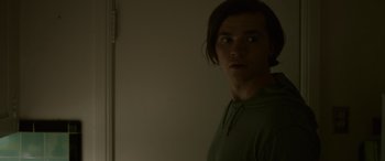 Movie still from “Sick” (2022), directed by John Hyams – A man standing in a dark room with his head turned to the side; Close Up shot, Over the shoulder angle