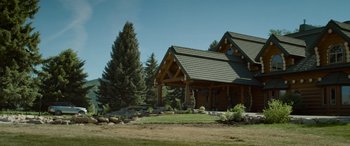 Movie still from “Sick” (2022), directed by John Hyams – A log cabin with a stone porch and a green tile roof; Extreme Wide shot, Low angle