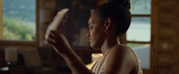 Movie still from “Sick” (2022), directed by John Hyams – A woman reading a paper in a room with a fireplace in the background; Close Up shot, Over the shoulder angle