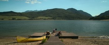 Movie still from “Sick” (2022), directed by John Hyams – A man kneeling down on a dock next to a lake; Extreme Wide shot, High angle