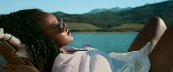 Movie still from “Sick” (2022), directed by John Hyams – A woman with sunglasses is laying on the ground by a body of water; Medium shot, Low angle