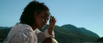 Movie still from “Sick” (2022), directed by John Hyams – A woman sitting on the side of a hill holding a pair of sunglasses; Close Up shot, Low angle