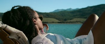 Movie still from “Sick” (2022), directed by John Hyams – A woman with a glass of water looking out at a lake; Medium shot, Over the shoulder angle