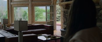 Movie still from “Sick” (2022), directed by John Hyams – A living room filled with furniture next to a fire place; Wide shot, Over the shoulder angle