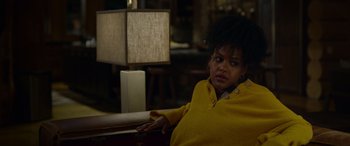 Movie still from “Sick” (2022), directed by John Hyams – A woman sitting in a chair in front of a lamp; Medium shot, Over the shoulder angle