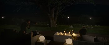 Movie still from “Sick” (2022), directed by John Hyams – A fire pit in the middle of a patio area at night; Extreme Wide shot, High angle