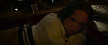 Movie still from “Sick” (2022), directed by John Hyams – A woman sitting in front of a window with her head resting on a pillow; Close Up shot, High angle