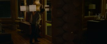 Movie still from “Sick” (2022), directed by John Hyams – A man standing next to a window in a room; Wide shot, High angle