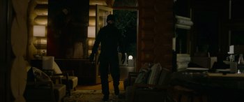 Movie still from “Sick” (2022), directed by John Hyams – A man in a black jacket is walking in a dark room; Wide shot, Low angle
