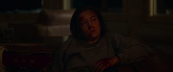 Movie still from “Sick” (2022), directed by John Hyams – A woman with a bruised face sitting on a couch; Medium shot, High angle