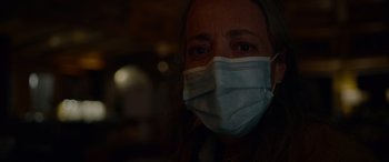 Movie still from “Sick” (2022), directed by John Hyams – A woman wearing a face mask in a dark room; Close Up shot, Over the shoulder angle