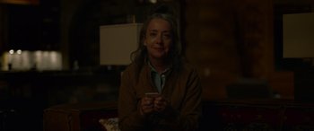 Movie still from “Sick” (2022), directed by John Hyams – A woman sitting on a couch holding a cell phone; Close Up shot, Over the shoulder angle