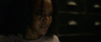 Movie still from “Sick” (2022), directed by John Hyams – A young woman with long black curly hair looking at the camera; Close Up shot, Over the shoulder angle