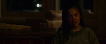 Movie still from “Sick” (2022), directed by John Hyams – A woman sitting on a couch in a dark room; Close Up shot, Over the shoulder angle