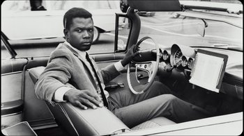 Movie still from “Sidney” (2022), directed by Reginald Hudlin – A black and white photo of a man sitting in the driver's seat of a car; Medium shot, Low angle