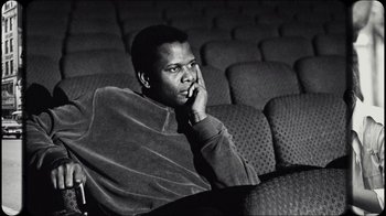 Movie still from “Sidney” (2022), directed by Reginald Hudlin – A black and white photo of a man sitting in a theater; Close Up shot, Low angle