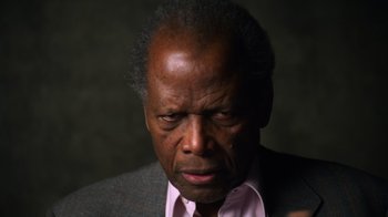 Movie still from “Sidney” (2022), directed by Reginald Hudlin – An older man wearing a pink shirt and a gray jacket; Close Up shot, Low angle