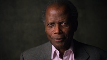 Movie still from “Sidney” (2022), directed by Reginald Hudlin – An older man wearing a suit and a pink shirt; Close Up shot, Low angle