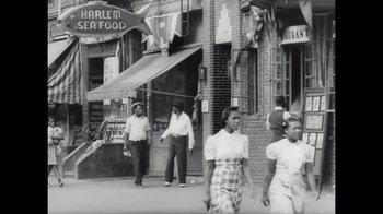Movie still from “Sidney” (2022), directed by Reginald Hudlin – A black and white photo of people walking down the street; Wide shot, Low angle