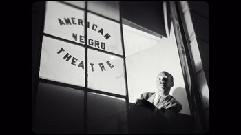Movie still from “Sidney” (2022), directed by Reginald Hudlin – A black and white photo of a man looking out of a window; Medium shot, Low angle
