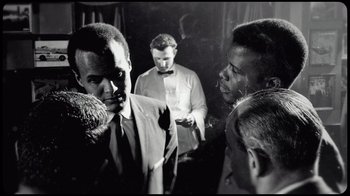 Movie still from “Sidney” (2022), directed by Reginald Hudlin – Black and white photograph of men in suits and ties talking; Medium shot, Over the shoulder angle